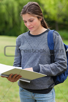 Young woman reading her notebook while standing up in a park