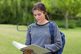 Young serious woman reading her notebook while standing in a par