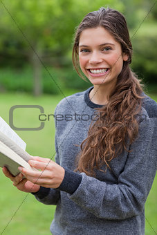 Young smiling girl looking at the camera while reading a book