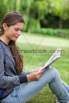 Young smiling woman reading a book while sitting on the grass in