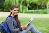 Young smiling girl reading a book while sitting on the grass
