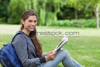Young smiling girl reading a book while sitting on the grass