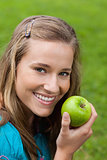 Attractive young girl eating a green apple in a park