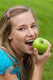 Young smiling woman looking at the camera while eating an apple