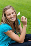 Young smiling woman holding a flower while sitting down