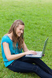 Young smiling girl typing on her laptop while sitting down on th