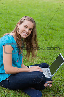 Young smiling girl looking at the camera while using her laptop