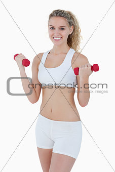 Young attractive woman smiling while lifting red weights