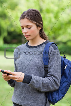 Young serious girl sending a text while standing in the countrys