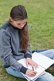Young serious girl doing her homework while sitting on the grass