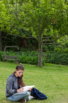 Young serious girl doing her homework while sitting down in a pa