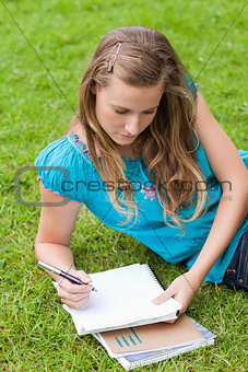 Young serious girl lying on the grass in a park while writing on