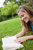 Young smiling woman reading a book while lying in a parkland