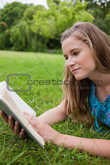 Serious young woman reading a book while lying on the grass