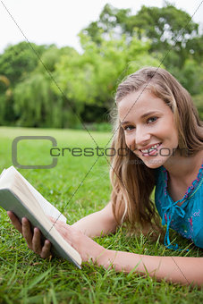 Smiling teenage girl holding a book in a parkland while looking 