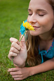 Young relaxed girl smelling a flower while lying on the grass