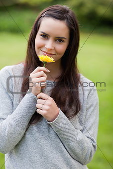 Young relaxed woman smelling a yellow flower while standing in a