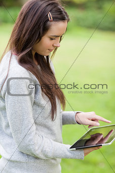 Young relaxed girl standing upright in a park while holding a ta