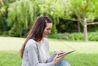 Young relaxed woman sitting in a park while using her tablet pc
