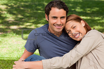 Man smiling as his friend rests his rests her head on his should