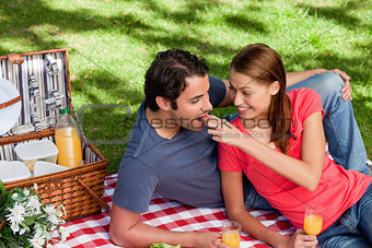 Young woman feeding her friend as they as they lie on a blanket 