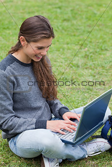 Smiling student typing on her laptop while sitting down on the g