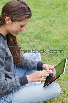 Young smiling adult sitting cross-legged in a park while using h