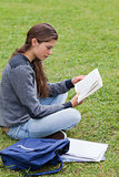 Young serious girl reading a book while sitting cross-legged