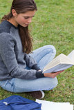 Relaxed young girl reading a book while sitting on the grass
