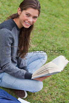 Young smiling woman sitting cross-legged in a park while holding