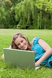 Young smiling girl using her laptop while lying on the grass