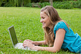 Young smiling girl looking at her laptop while lying down