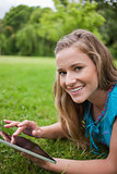 Smiling young woman lying down in a parkland while using her tab