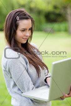 Young relaxed woman holding her laptop while standing in a park