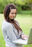 Smiling young woman holding her laptop while standing in a publi