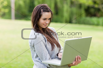 Serious young woman standing upright in a park while holding her