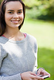 Smiling young woman using her cellphone while standing in a park