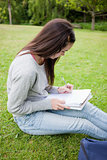 Young serious student sitting in a park while writing on a noteb