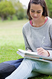 Young smiling girl writing on her notebook while sitting in a pa