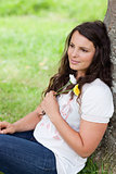 Young relaxed woman sitting against a tree while holding flowers