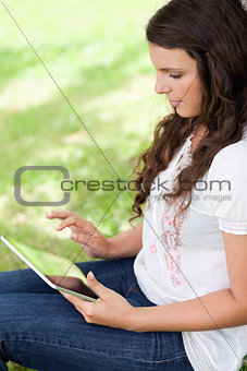 Young woman sitting in the countryside while using her tablet pc