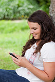 Young relaxed woman sending a text while sitting against a tree
