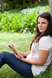 Young relaxed woman looking at the camera while holding a book