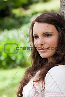 Young peaceful woman leaning against a tree while looking toward