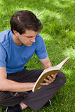 Young serious man sitting cross-legged while reading a book
