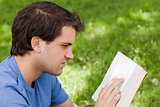 Young serious man reading a book while sitting in a park