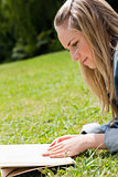 Young blonde girl lying on the grass while reading a book