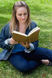 Young relaxed girl reading a book while sitting on the grass