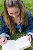 Young relaxed girl lying on the grass while reading a book
