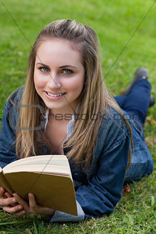 Young happy girl lying on the grass while holding a book and loo